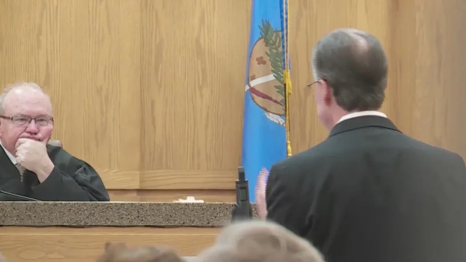 Judge Olsen sits in the courtroom next to a flag of Oklahoma