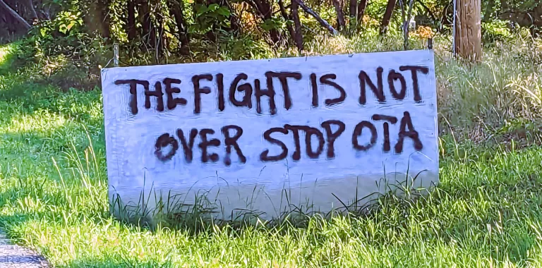 A spray painted wooden sign reads "The fight is not over stop OTA"