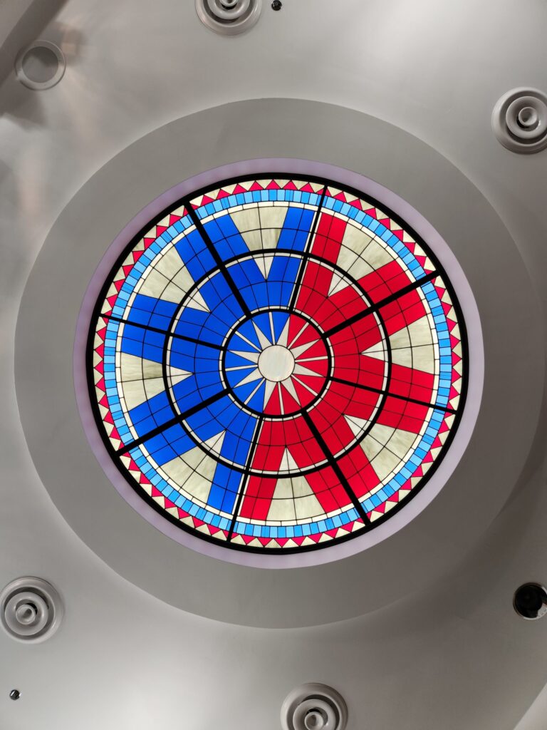 A red and blue stained glass circle of the seal of the City Of Norman Oklahoma